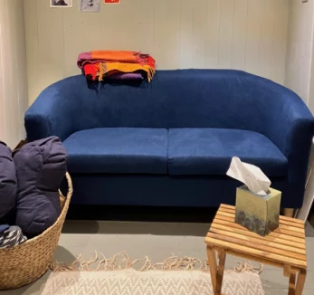 Photograph of a small sofa against a wall inside a room with a blanket on the arm