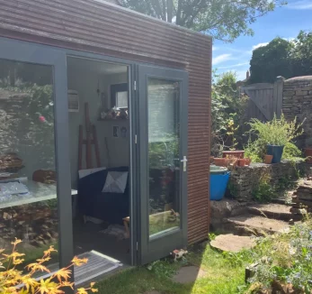 Photograph of a wooden building in a garden with open doors